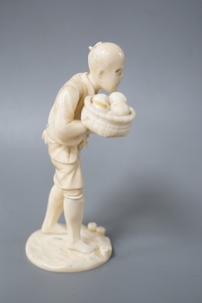 A Japanese carved ivory figure, Meiji period, modelled as a fruit vendor carrying a bowl of fruit in one hand and a piece of fruit in the other, standing on a naturalistic circular base, signed on base, height 14.5cm